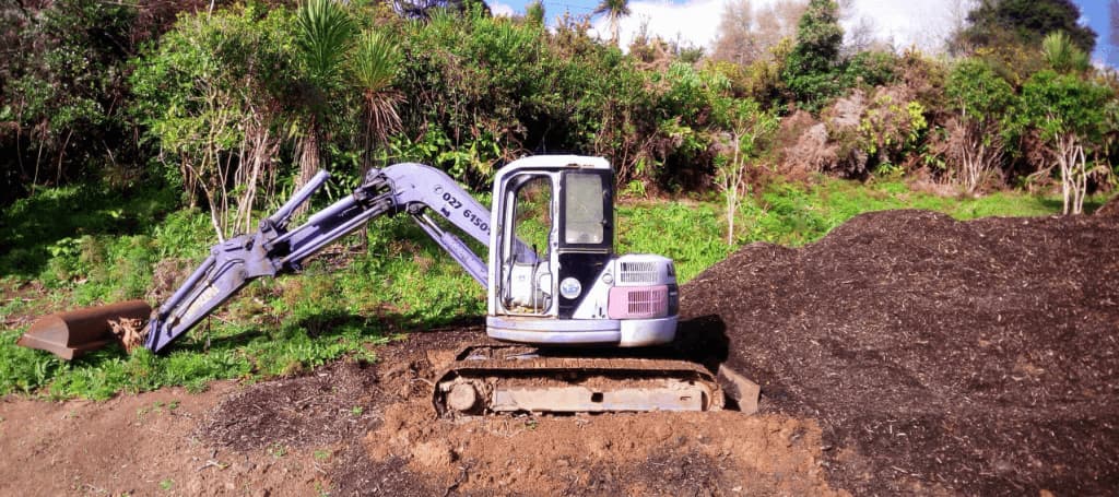 Small blue digger in a resting position on site with a recently moved pile of earth behind it