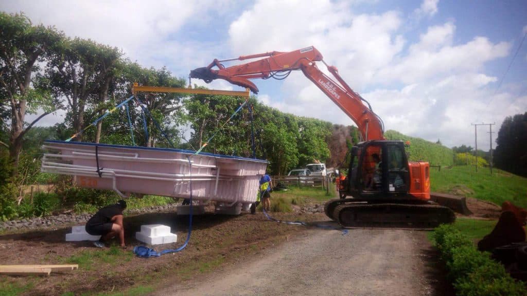 Orange digger lifting a pool down in to a recently excavated hole