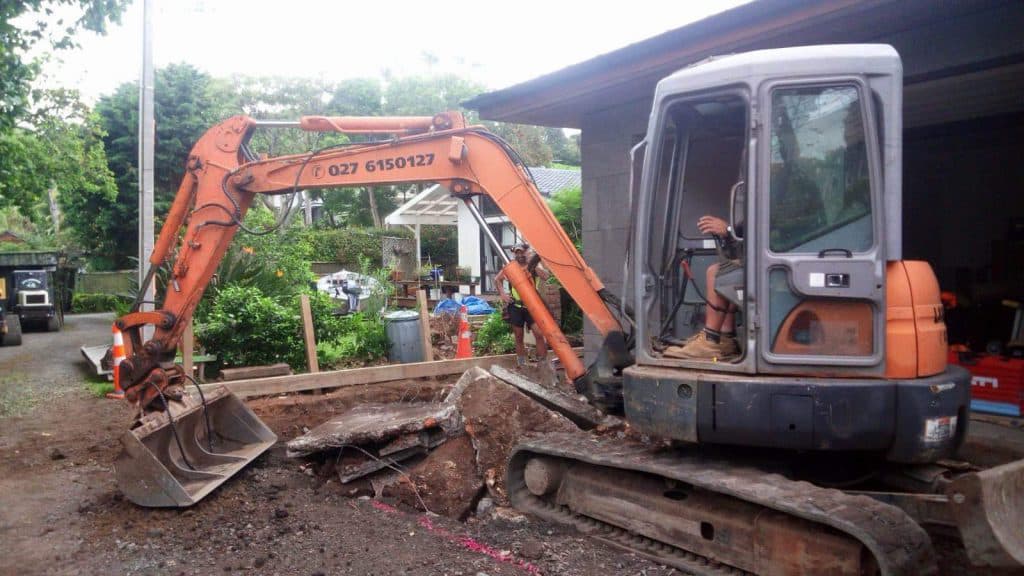 Small orange digger excavating a hole in an Auckland resident's backyard for a new pool