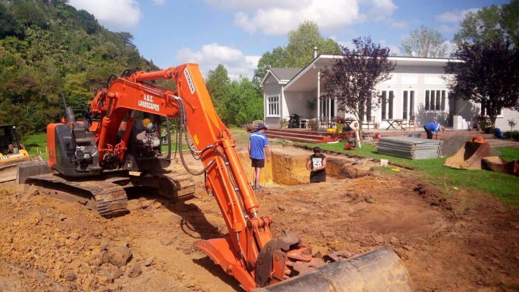 The ABC Excavation and landscaping team with a Vibrant orange digger excavating earth in a residential property's backyard