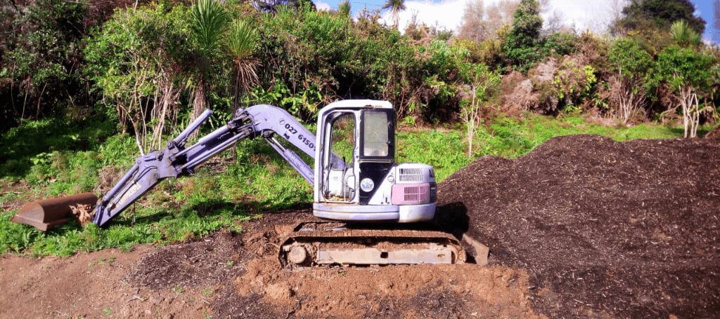 Small blue digger in a resting position on site with a recently moved pile of earth behind it