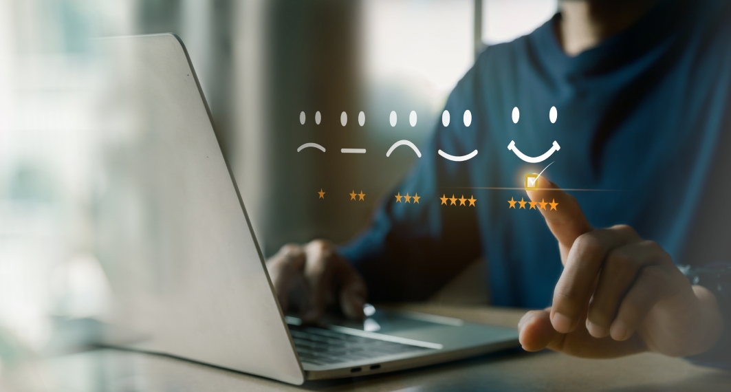 Man sitting at a desk with one hand on a laptop and the other pointing at a 5 star rating with a smiley face