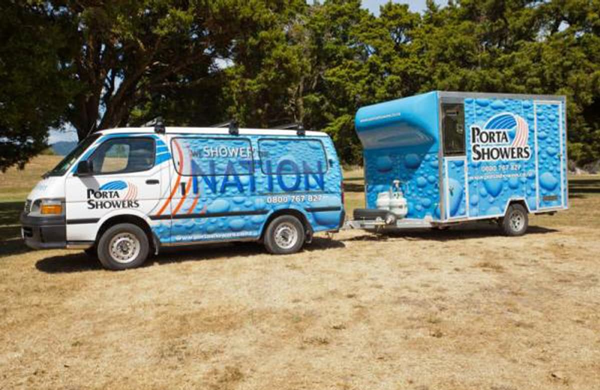 Porta Shower van towing a portable shower trailer unit parked in a dead grass field with trees covering the background