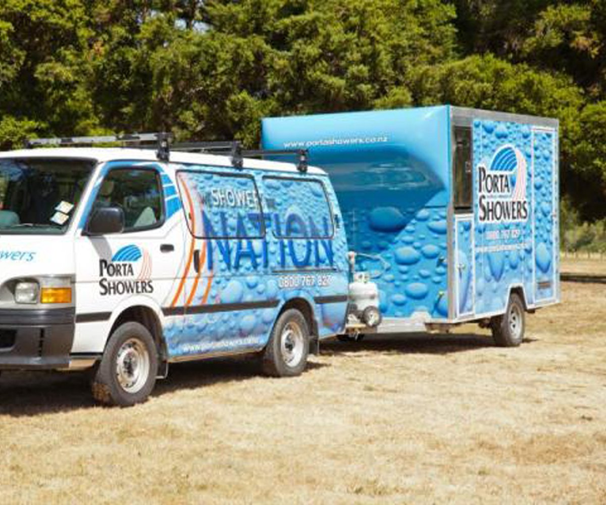 Porta Showers' Van towing a portable shower trailer unit parked in a dead grass field with trees covering the background