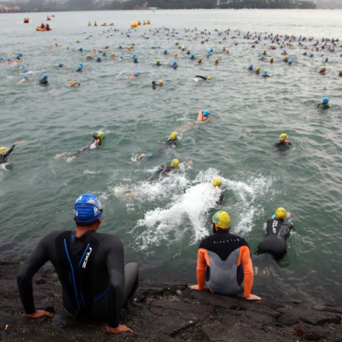 Hundreds of triathlon participants swimming in a lake, rushing to get in the water and get around a yellow buoy