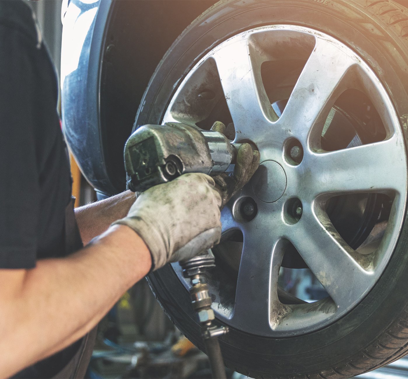 Expert automotive mechanic using an electric socket impact wrench on a car's wheel nuts