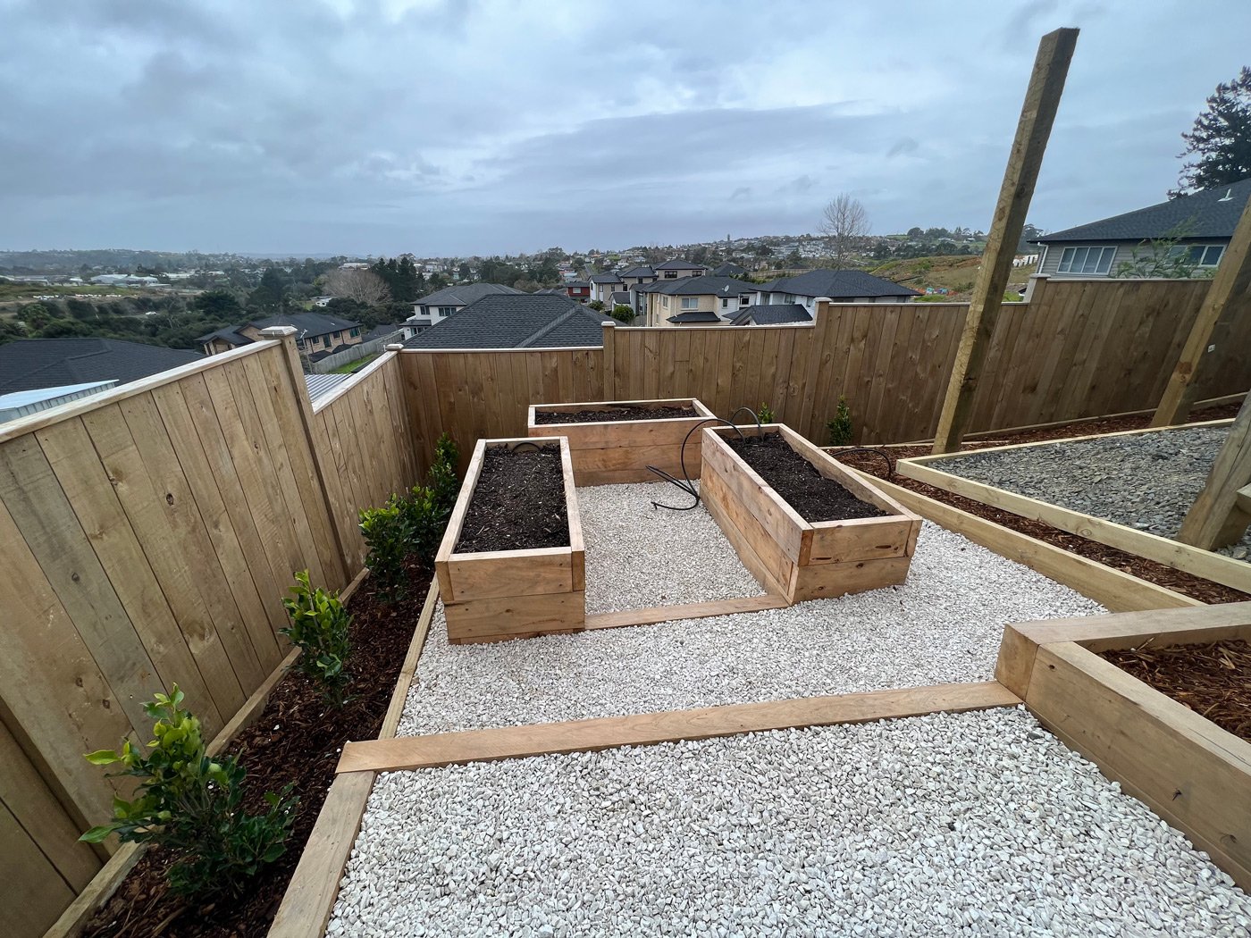 Three newly built vegetable beds raised off the ground in wood casings, surrounded by a white pebble walkway