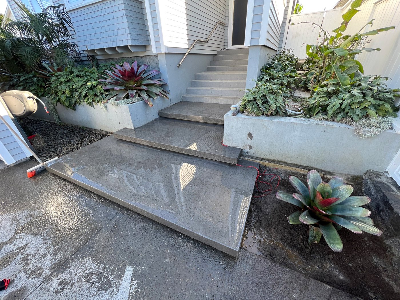 Freshly cleaned floating concrete front steps to a house with plants on the sides in the garden supported by a concrete retaining wall