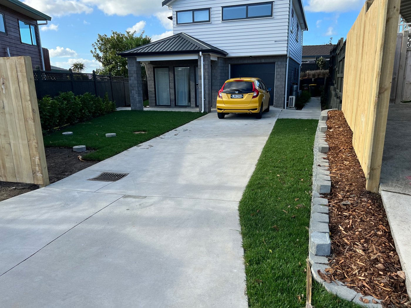 New build with a smooth concrete driveway with a grate for drainage and and a lively grass yard