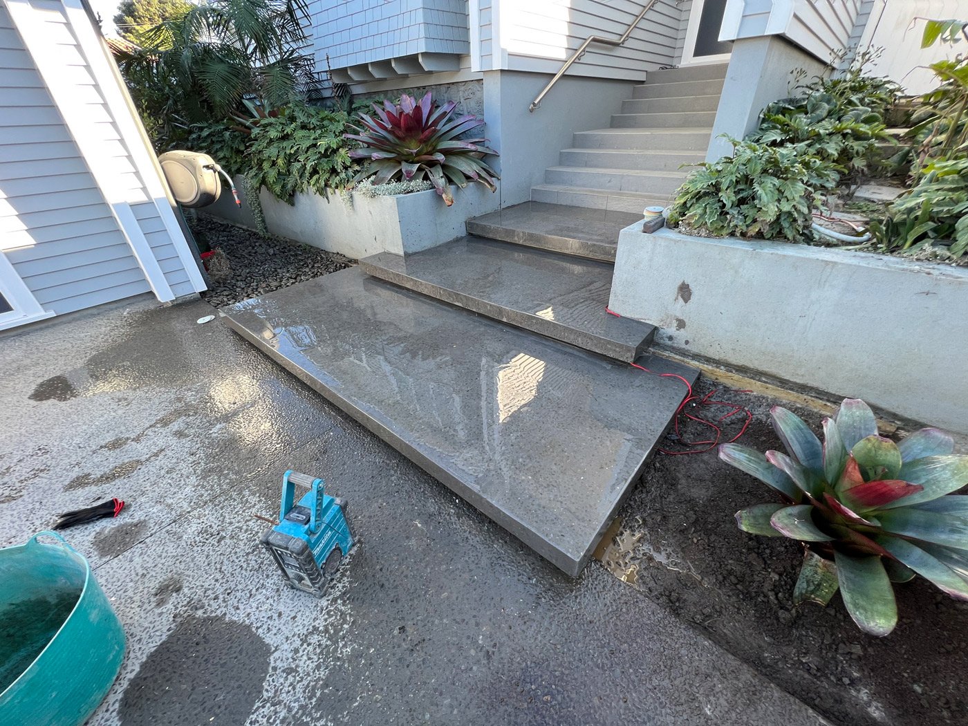 Freshly cleaned floating concrete front steps to a house with plants on the sides in the garden supported by a concrete retaining wall
