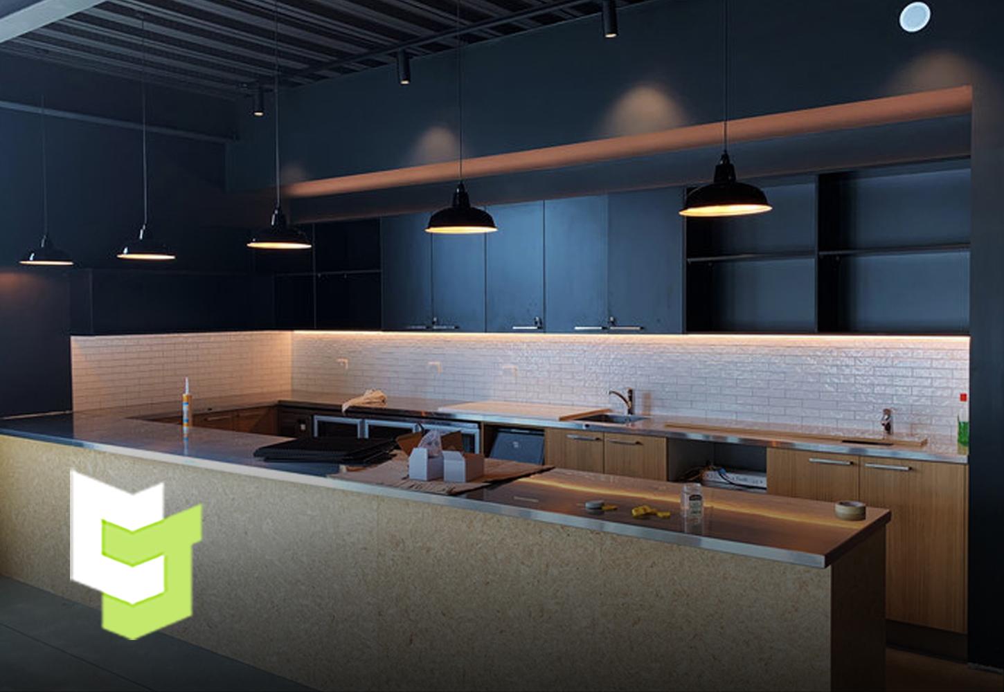 NZMA industrial kitchen space with sleek black hanging lights and a mixture of black and oak coloured wooden cabinetry 