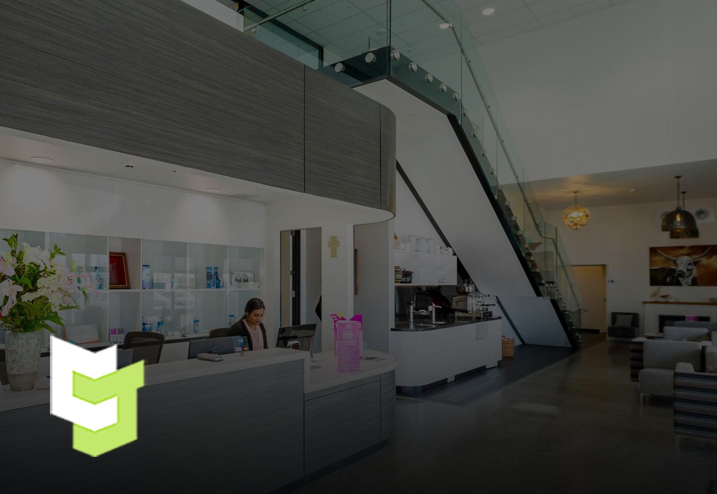 Hotel reception with white walls and ceilings and bright white lights, well-contrasted with Colourform Joinery's grey wood panels