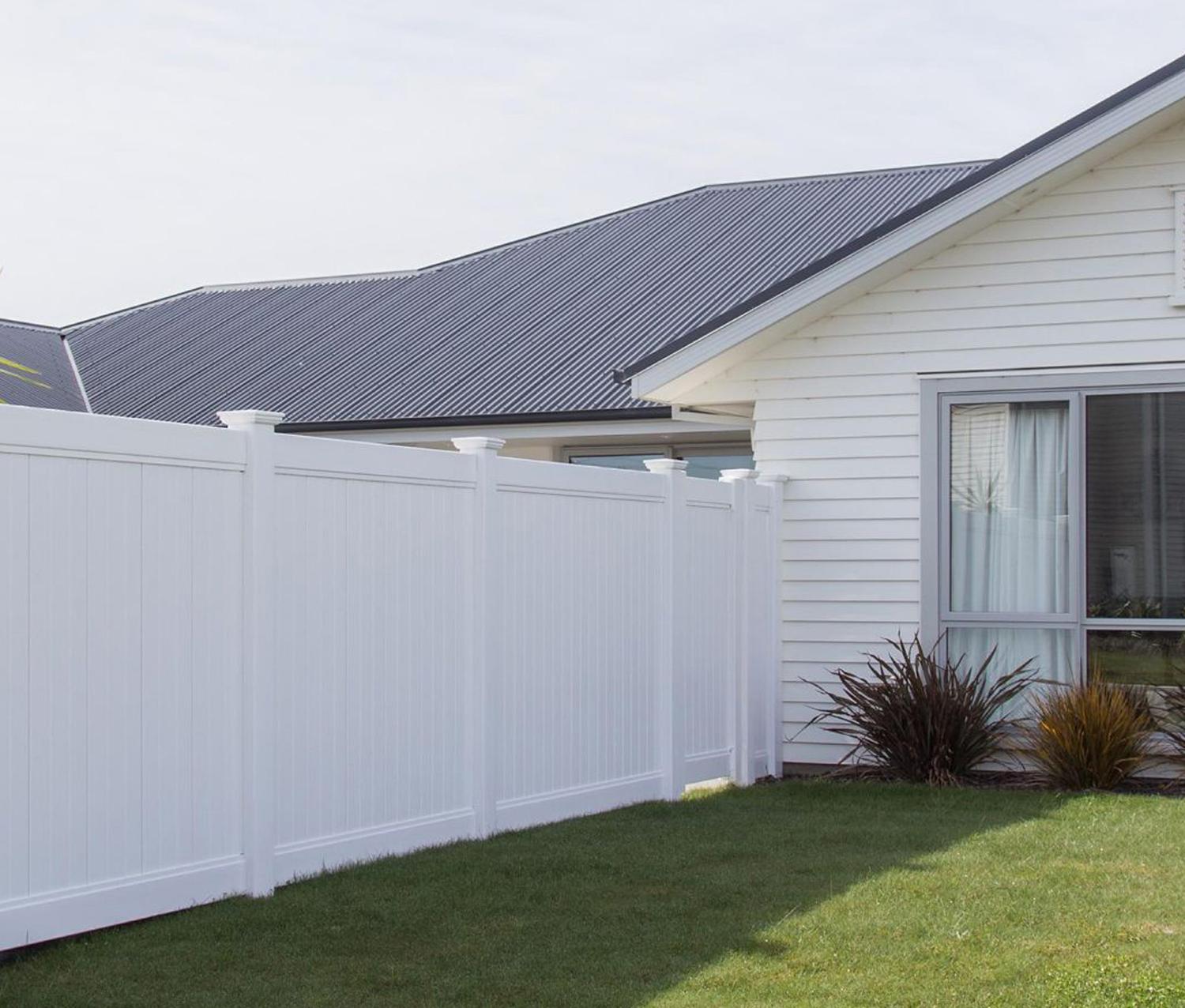 Grass section beside a white weatherboard home and a tall PVC fence that blocks off the backyard and windows
