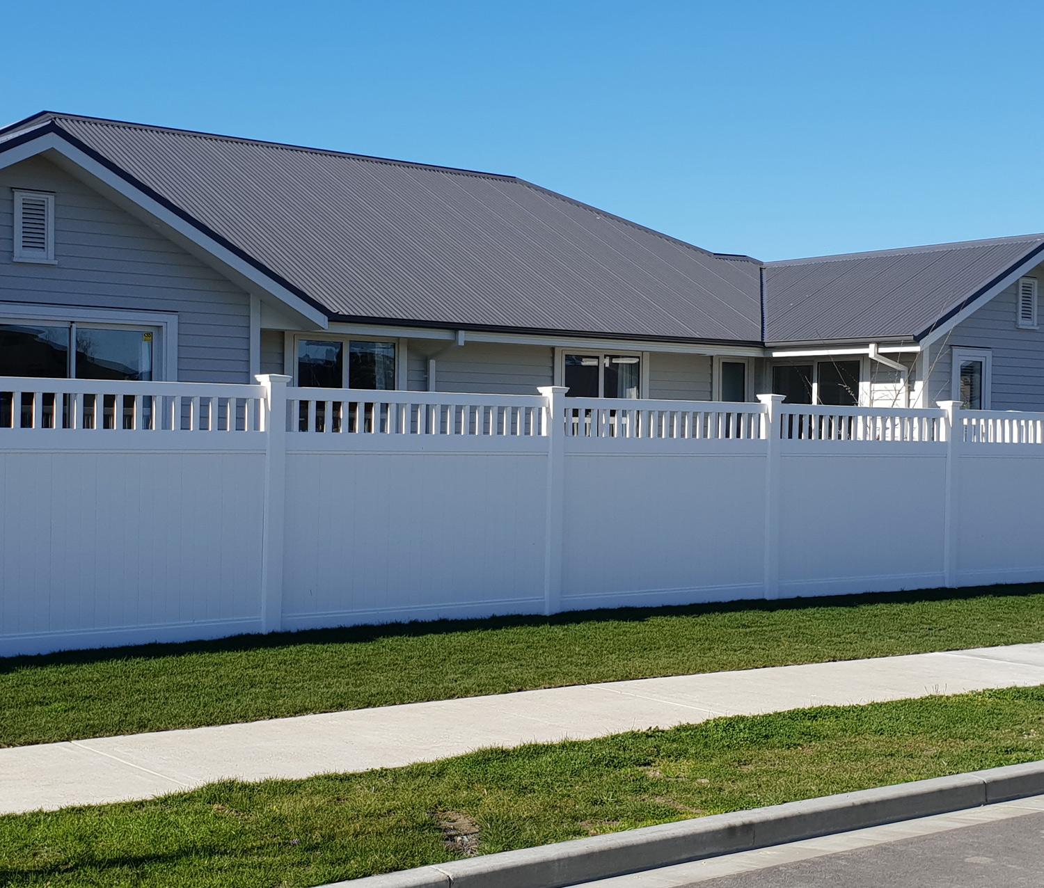Tall new white fence in front of a grey modern house with a tidy front lawn and recently poured footpath