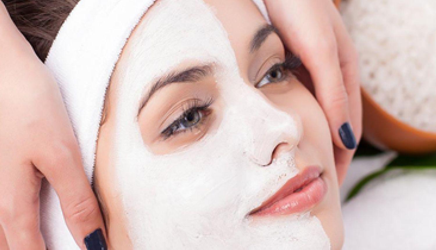 Woman laying back with half her face covered by a skincare mask product as she gets massaged by a facial expert