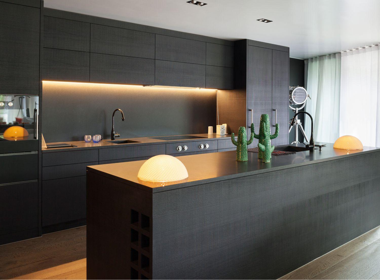 Dark black kitchen with cosy yellow lighting and a family of green cacti on the island bench
