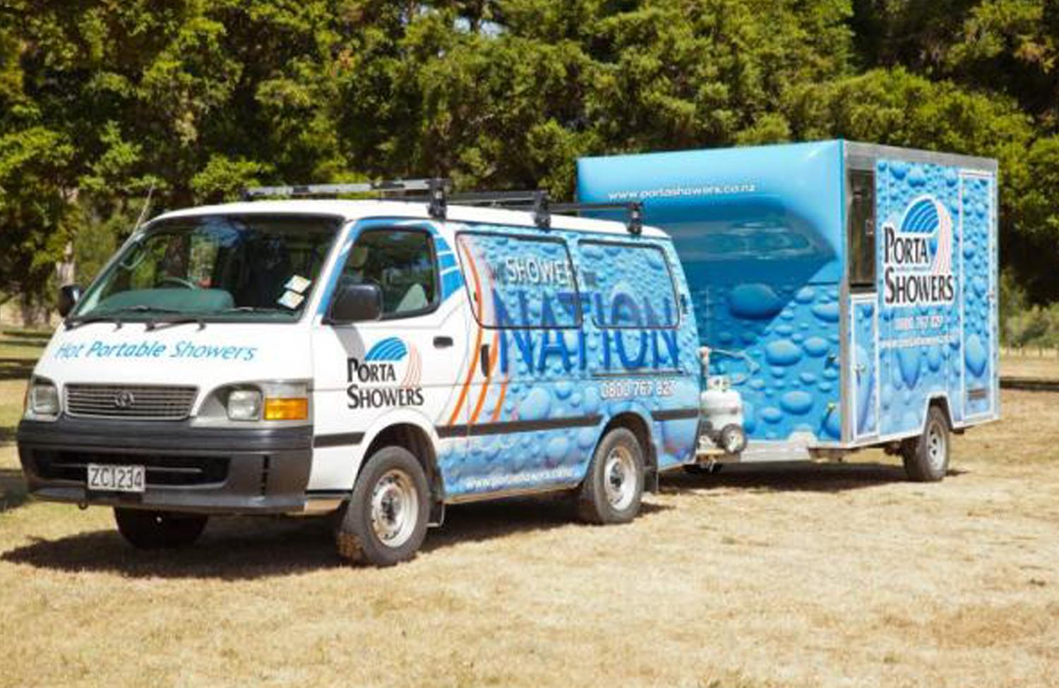 Porta Showers' Van towing a portable shower trailer unit parked in a dead grass field with trees covering the background