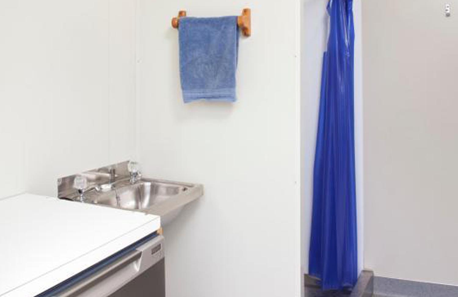 Interior of a Porta Showers' self-contained shower units with a sink, bench, towel rack, and a shower