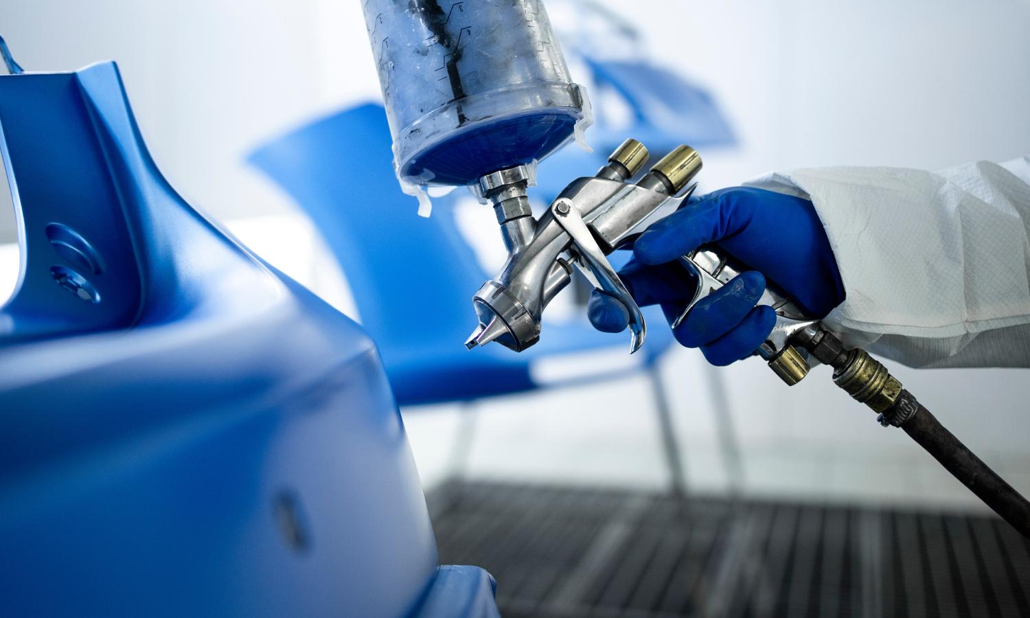 Person covered in a protective suit holding a paint spray gun as he sprays a car door blue