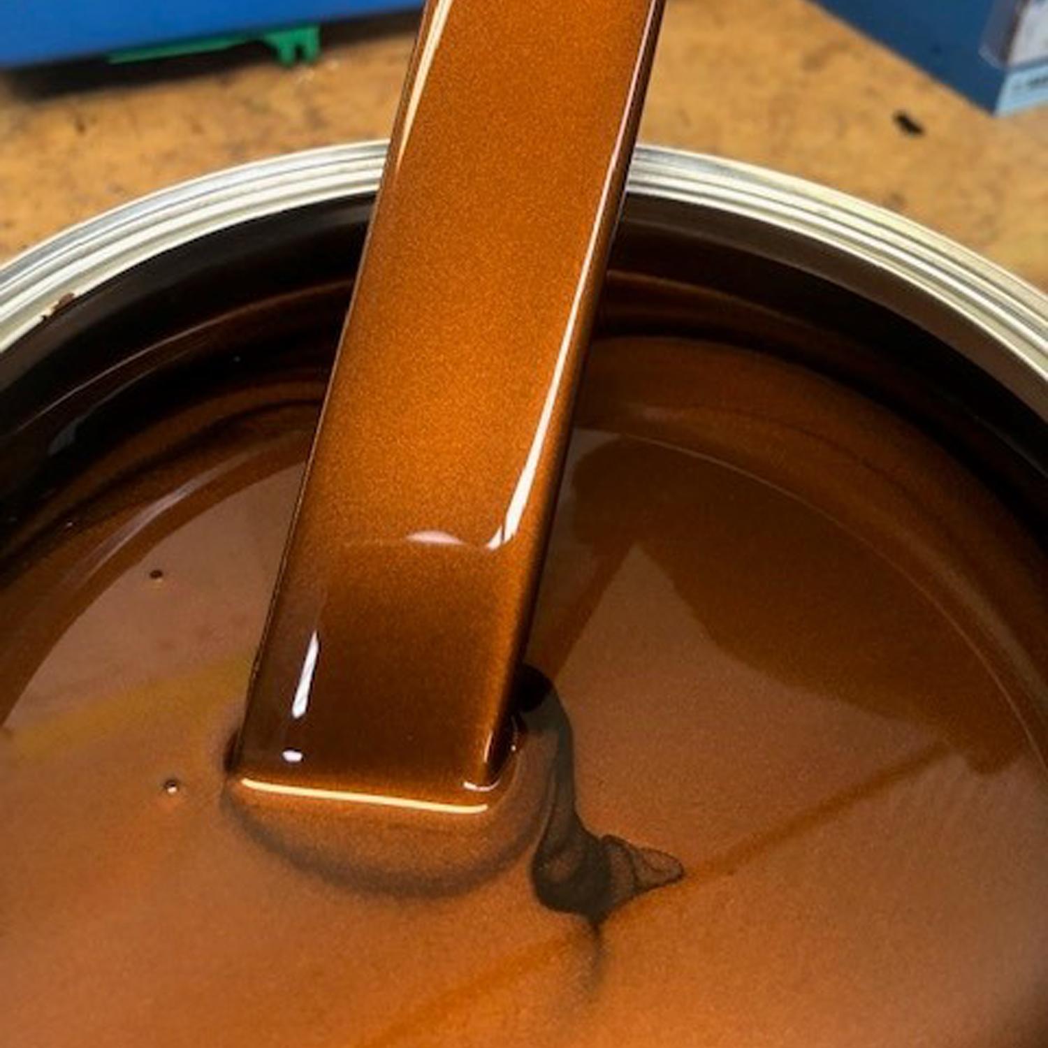 Orange rust-like coloured basecoat on a stick that's been dipped into a paint bucket