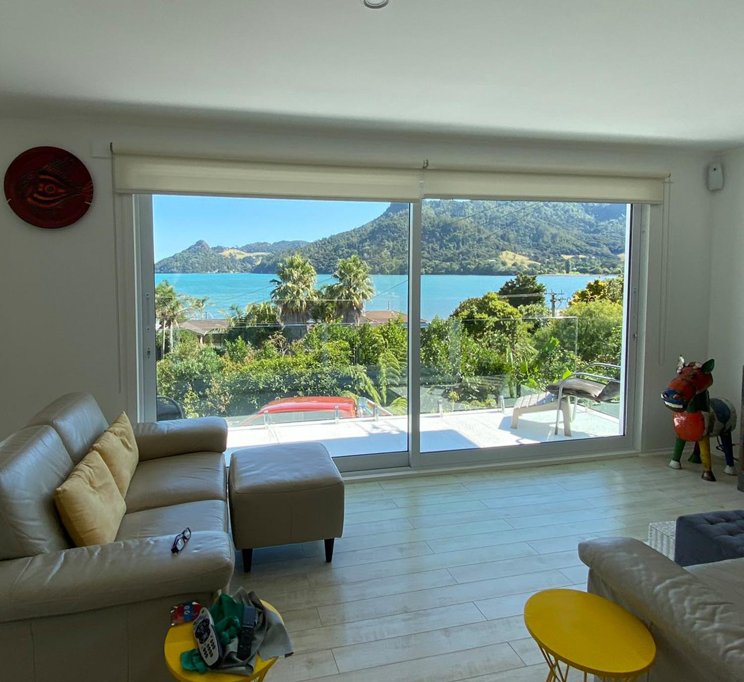 Inside a living room looking out through large thermally broken windows to a trees and a harbour