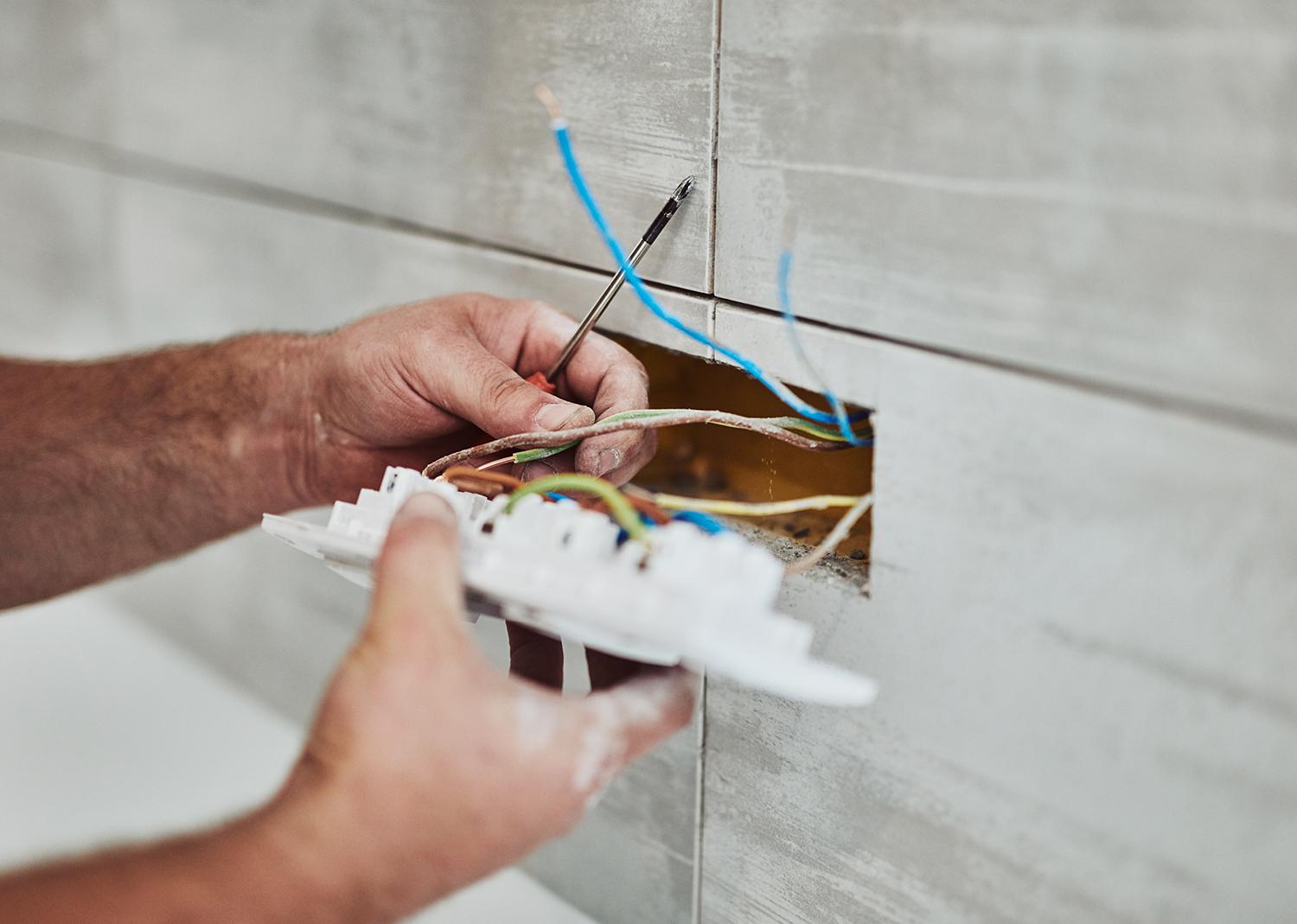 Close up of the hands of a male electrician installing a light switch socket - links to industrial electrical page