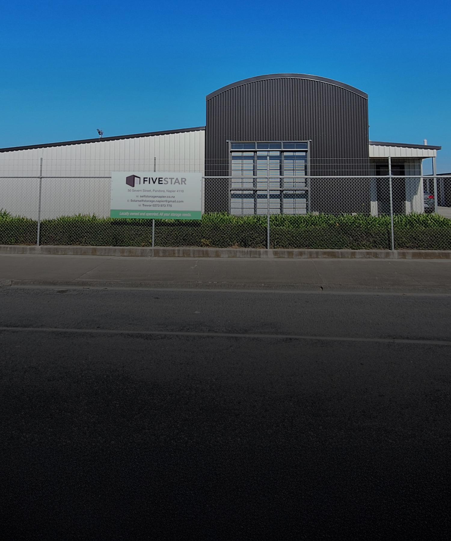 Photo outside the front of Five Star Self Storage Facility with their sign on the fence on a clear blue sky day | Links to the 'Who We Are' page