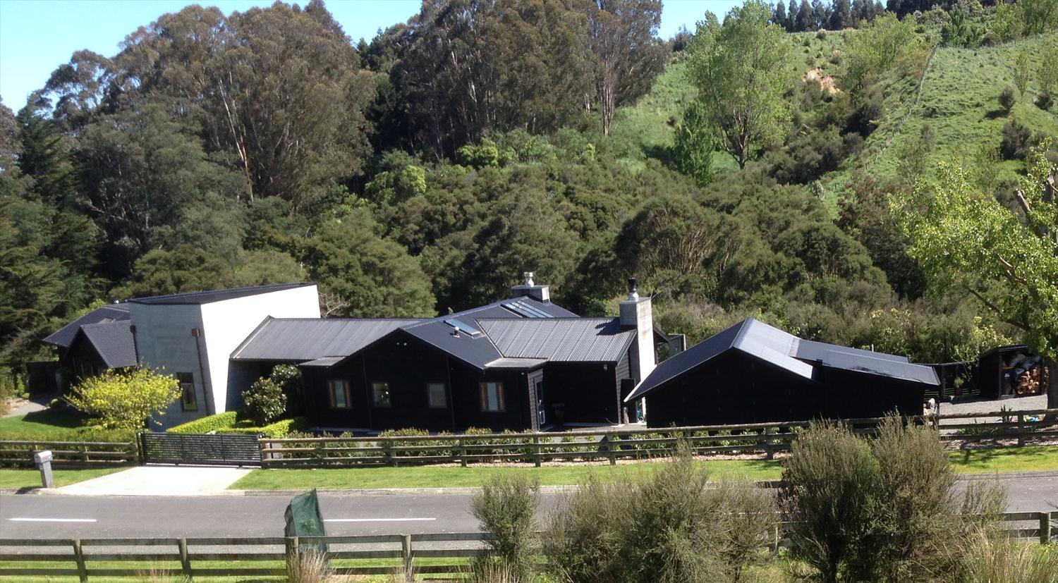 A rural house, modern and black with a hill and native bush behind it - links to Rural Septic Systems page