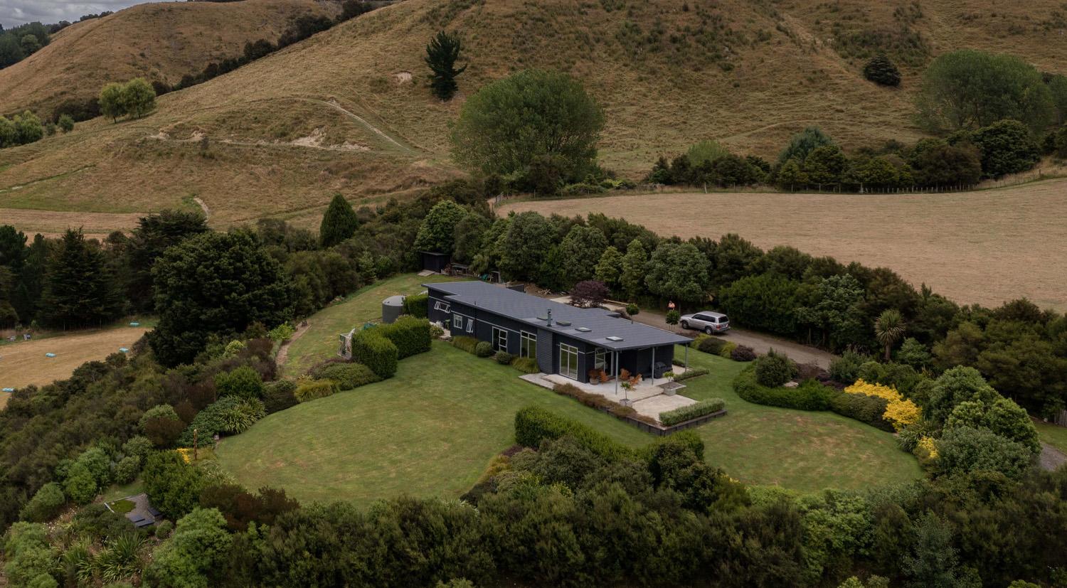 Aerial view of a rural house on a large lifestyle block with the house surrounded by a large circle of trees - links to the Case Studies page