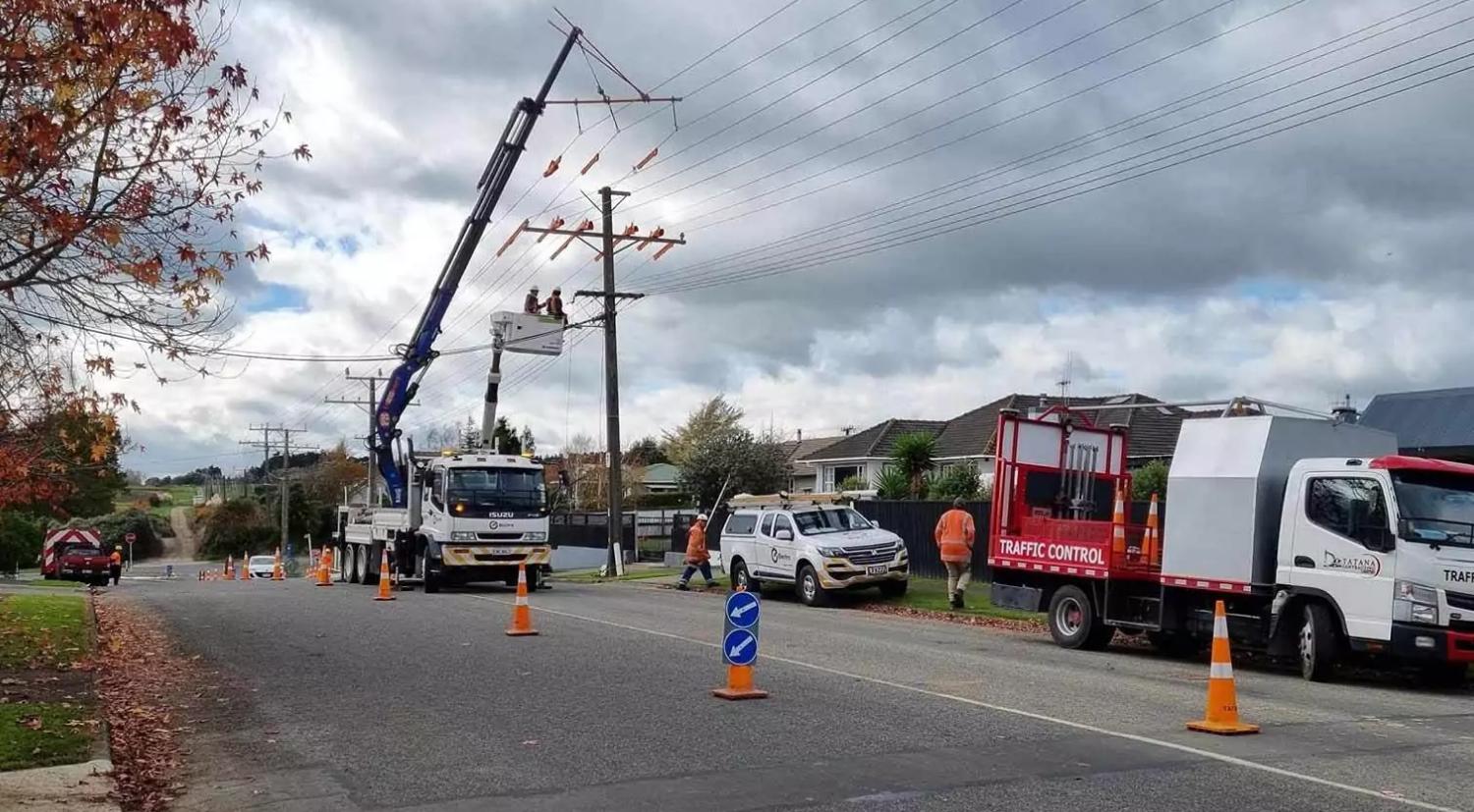 Image of people in a cherry picker working on powerlines while Tatana Contracting cone off the road | Temporary Traffic Management Manawatu