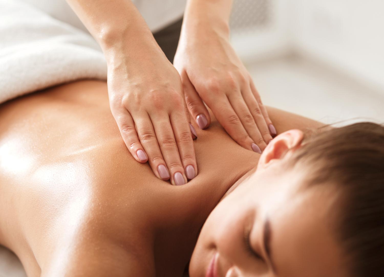 Close up view of a ladies hands massaging the top of a female patient's back - links to the 'Massage' page