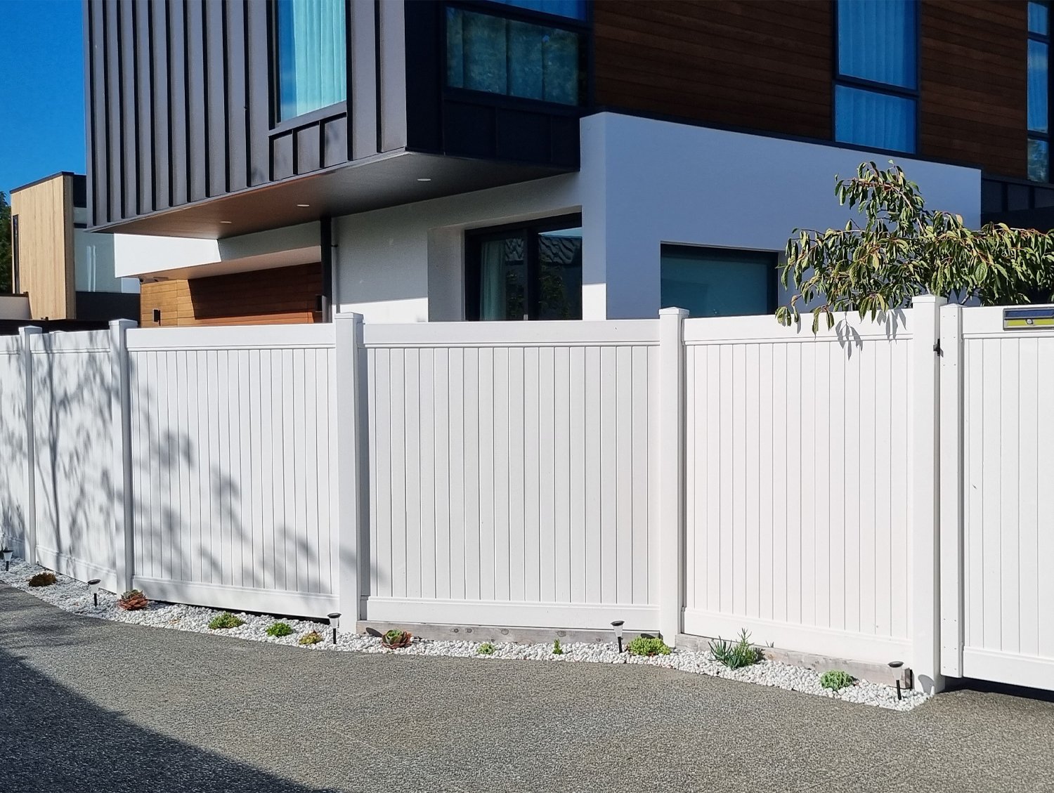 Modern white PVC fence with a textured concrete driveway in front of a modern container house