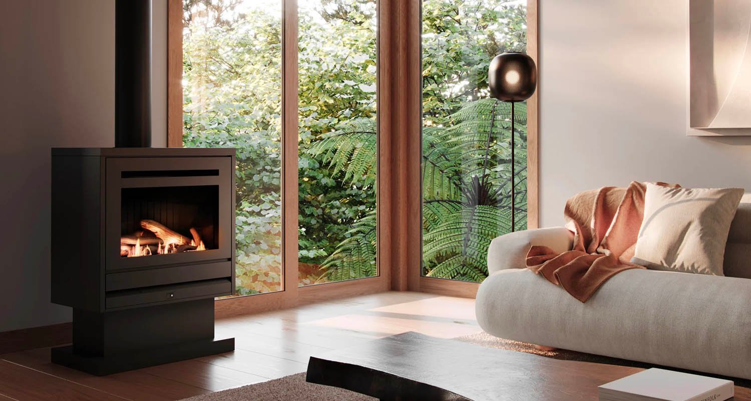 Freestanding wood fire in a living room with earthy tones and floor to ceiling windows that shows off the surrounding nature