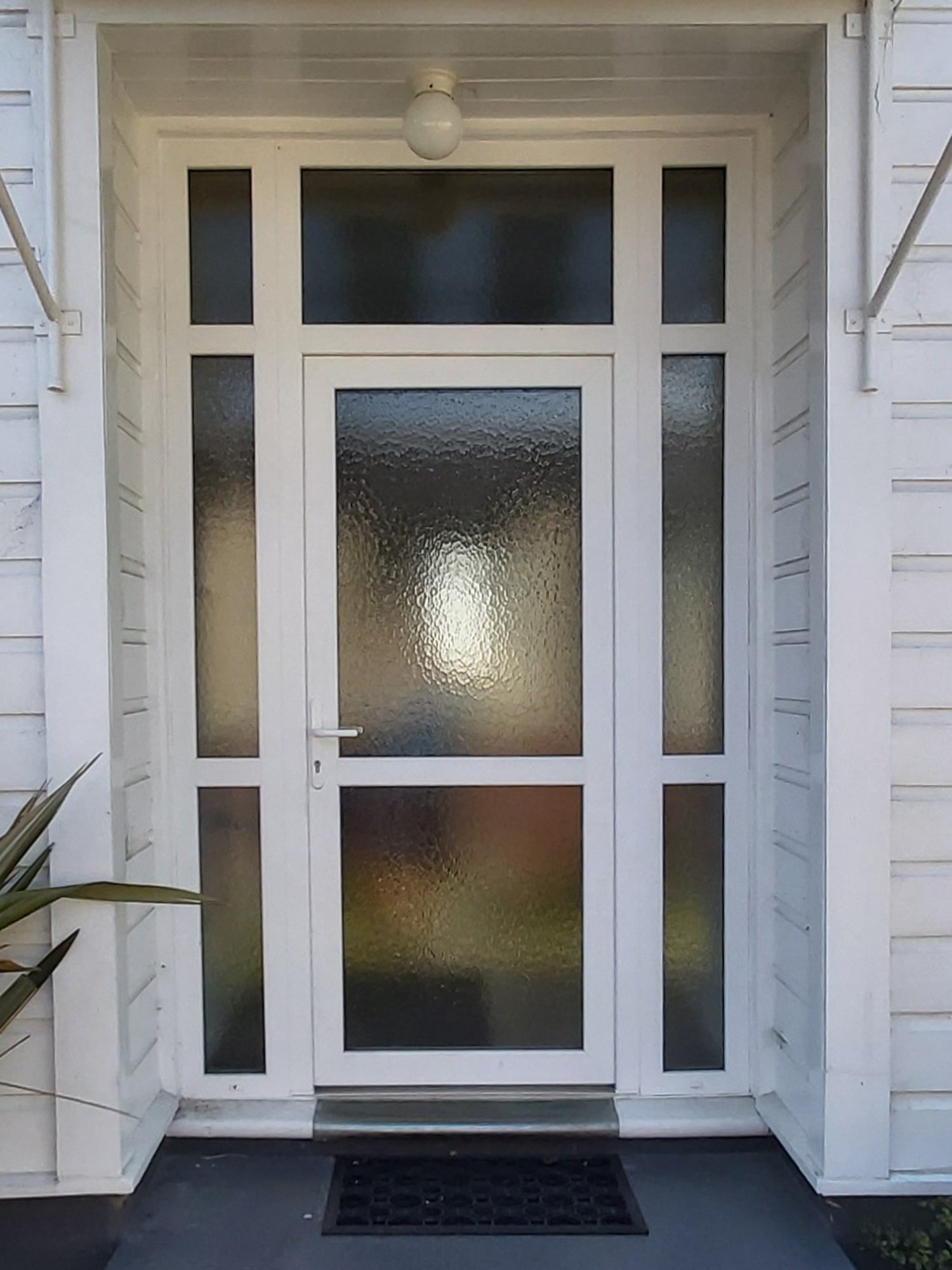 white weatherboard home with an old glass door and white uPVC framing around the windows and entrance