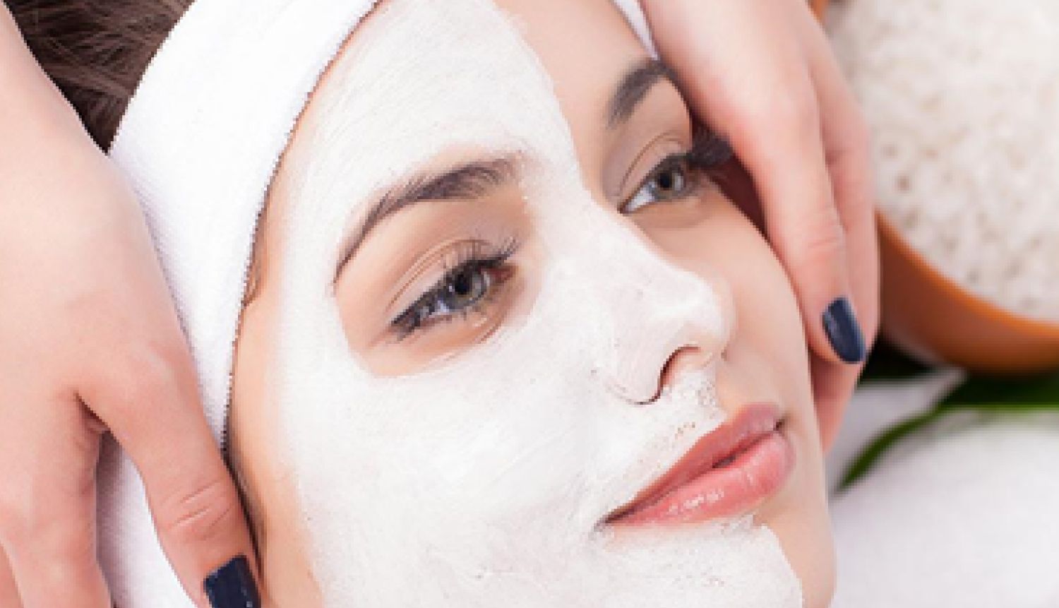 Woman laying back with half her face covered by a skincare mask product as she gets massaged by a facial expert
