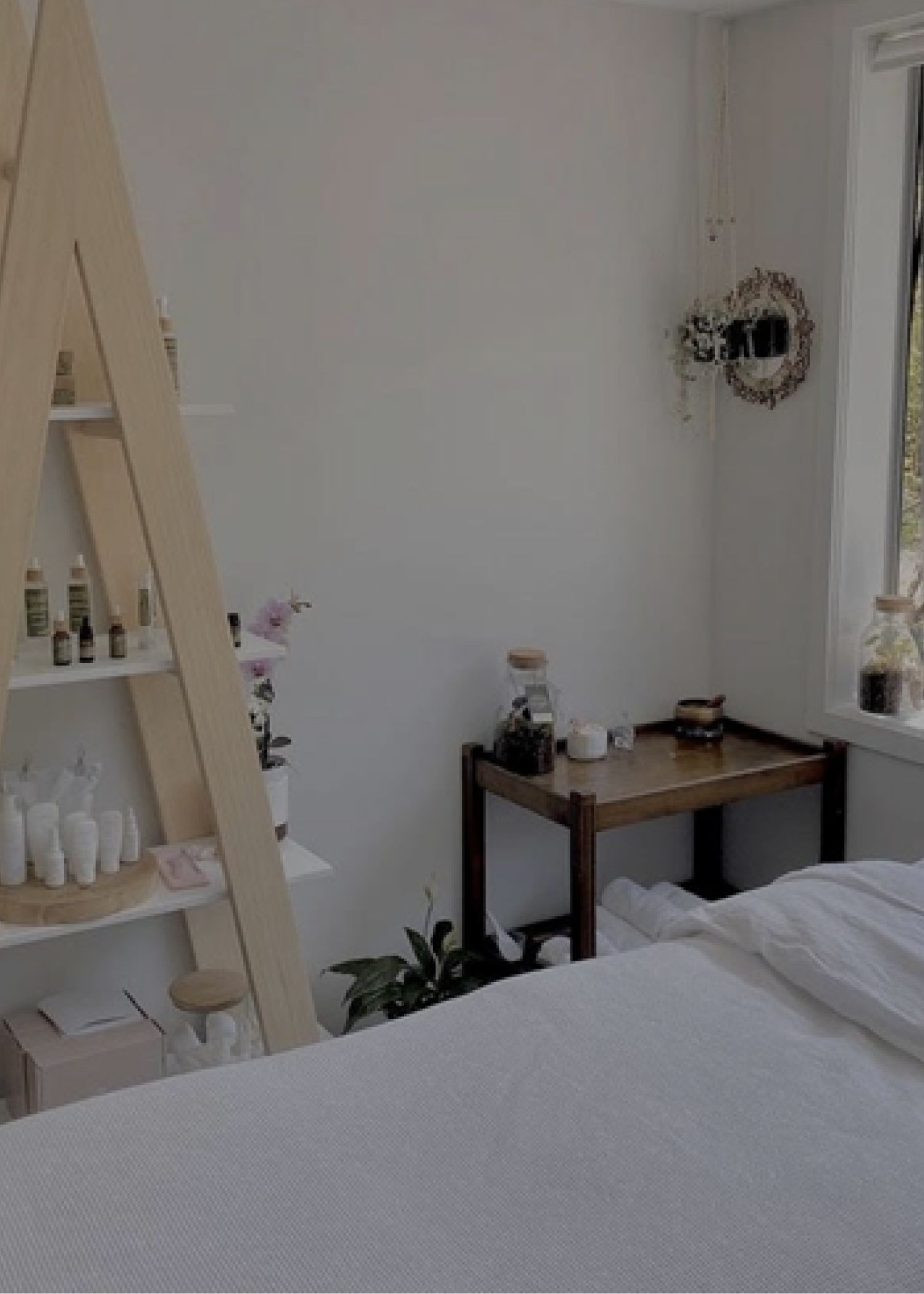 Spa bed with white sheets in a small white room with an open window and plenty of facial products on shelves