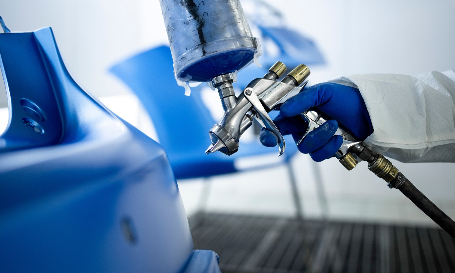 Person covered in a protective suit holding a paint spray gun as he sprays a car door blue