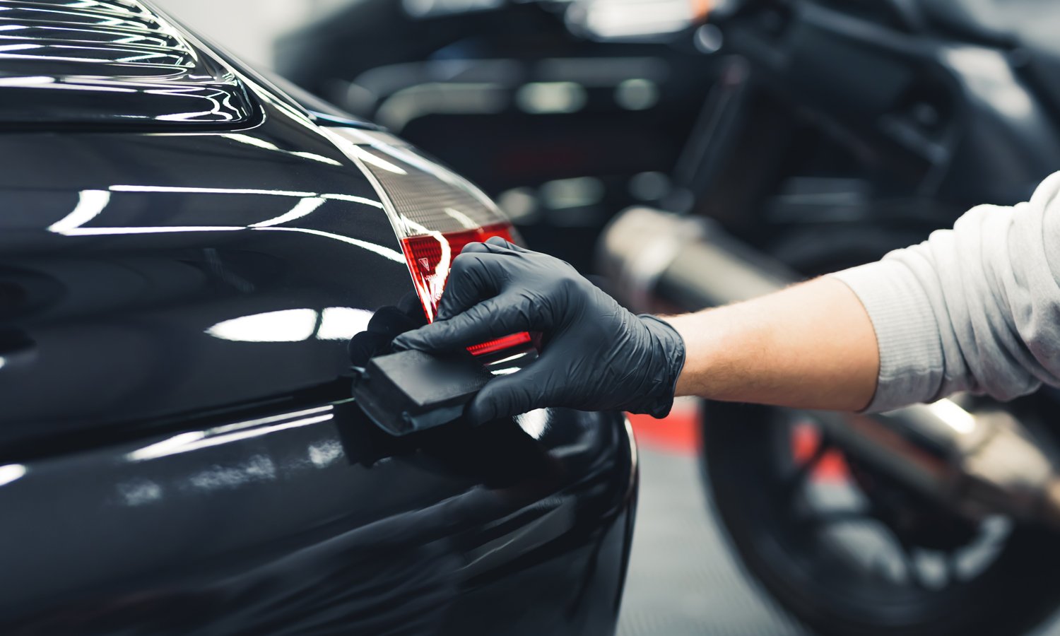 Man in black gloves wiping down the fine edges of a black vehicle
