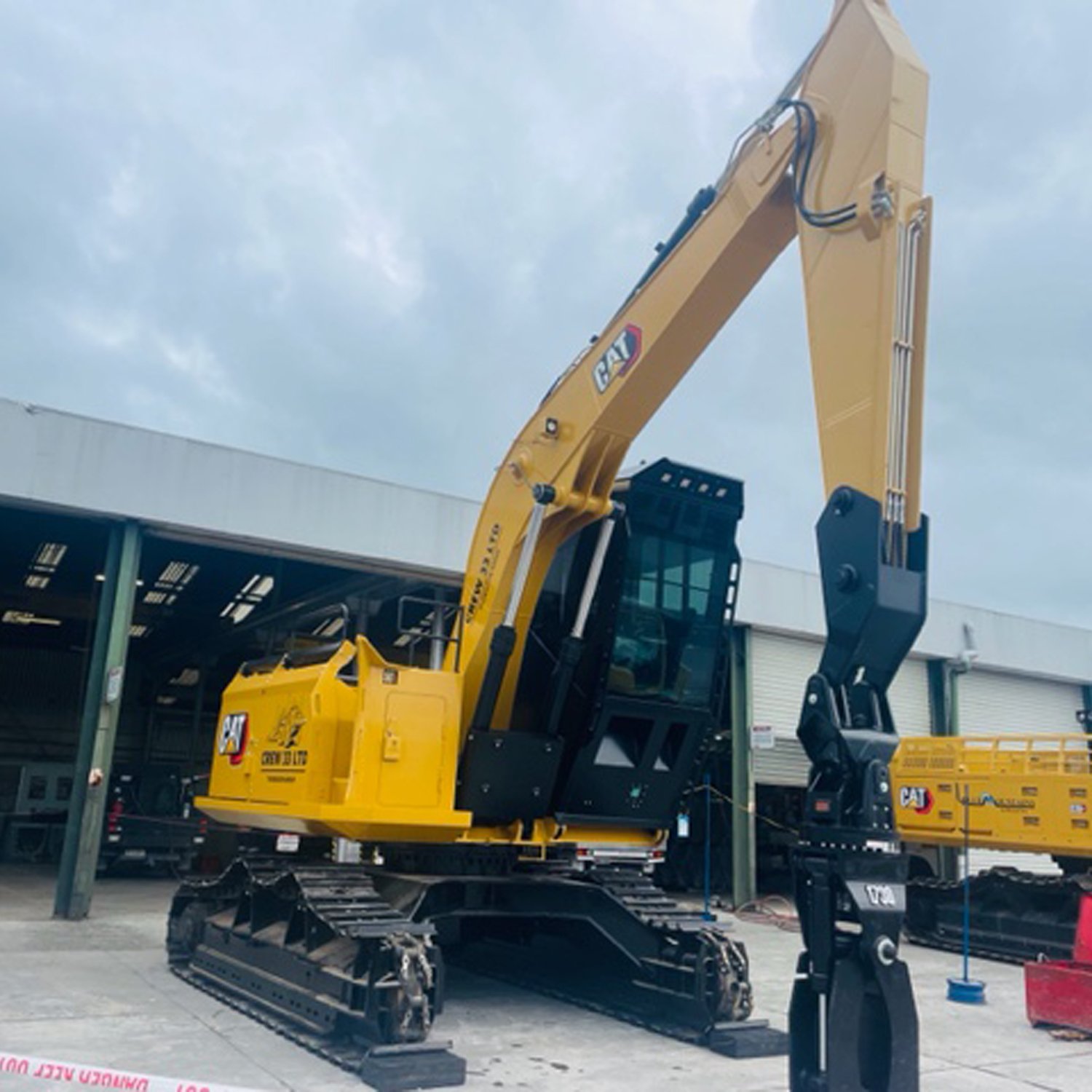 Big yellow industrial crane parked up in front of a rural warehouse with its claw bucket touching the ground