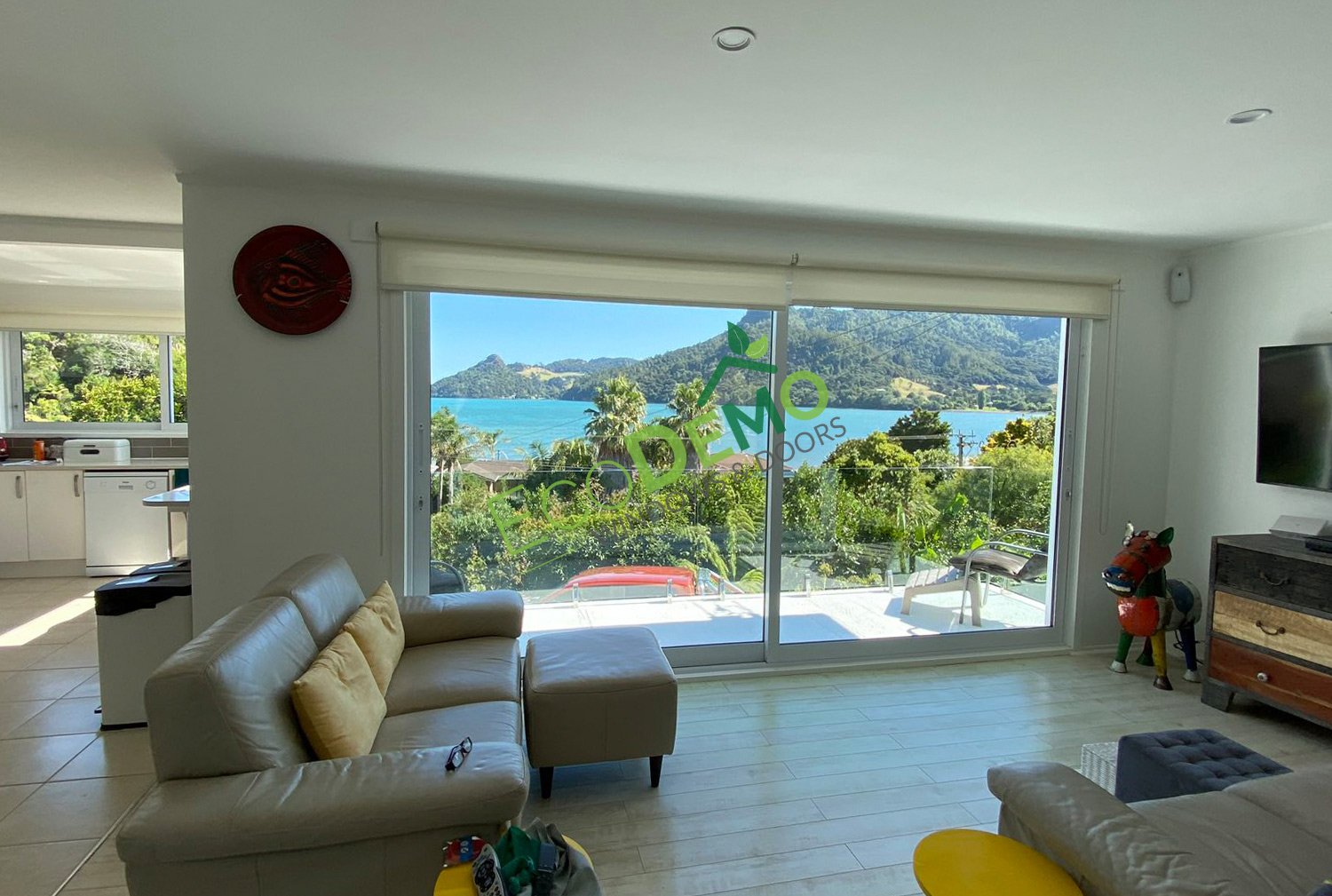 Inside a living room looking out through large thermally broken windows to a trees and a harbour