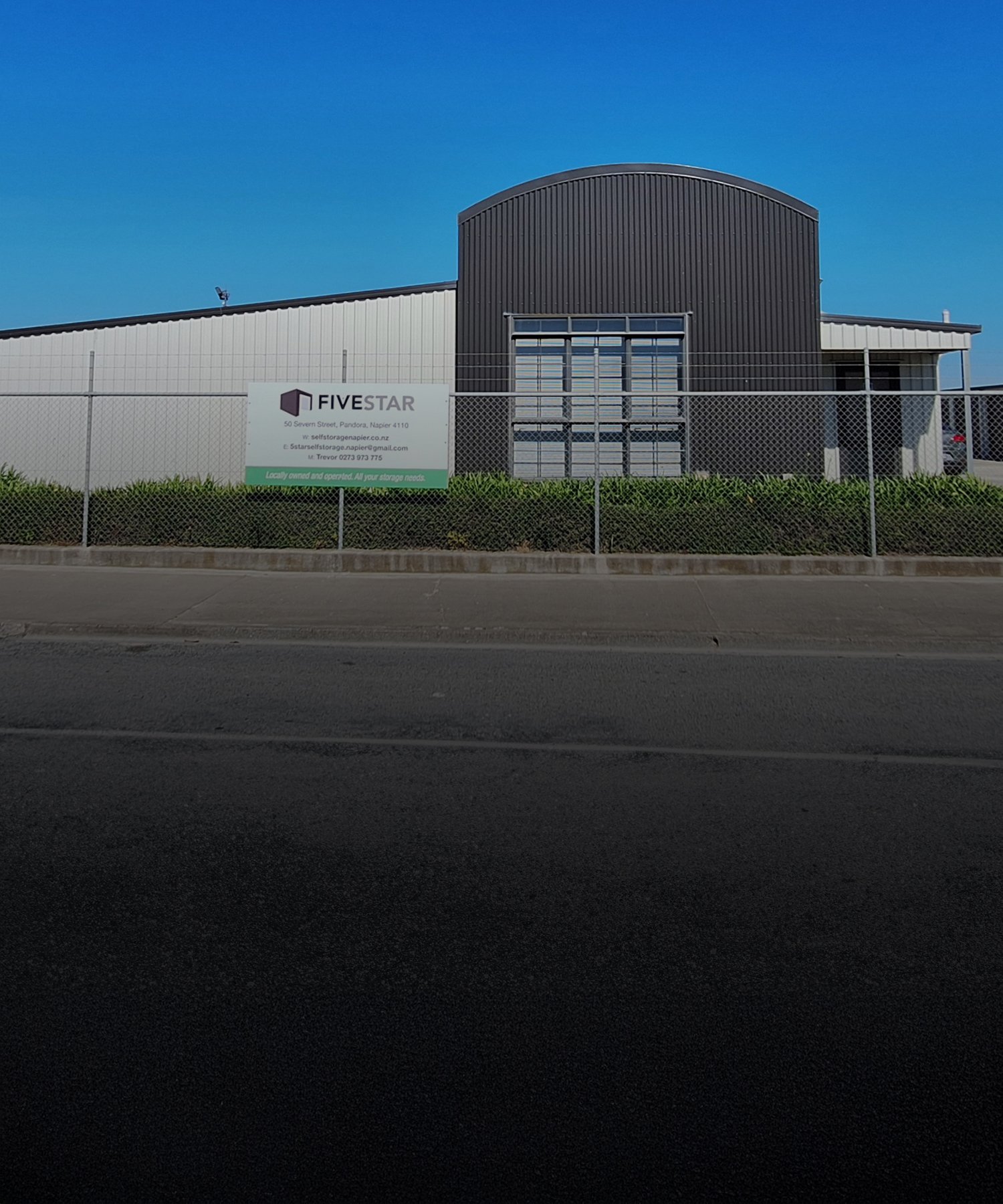 Photo outside the front of Five Star Self Storage Facility with their sign on the fence on a clear blue sky day | Links to the 'Who We Are' page