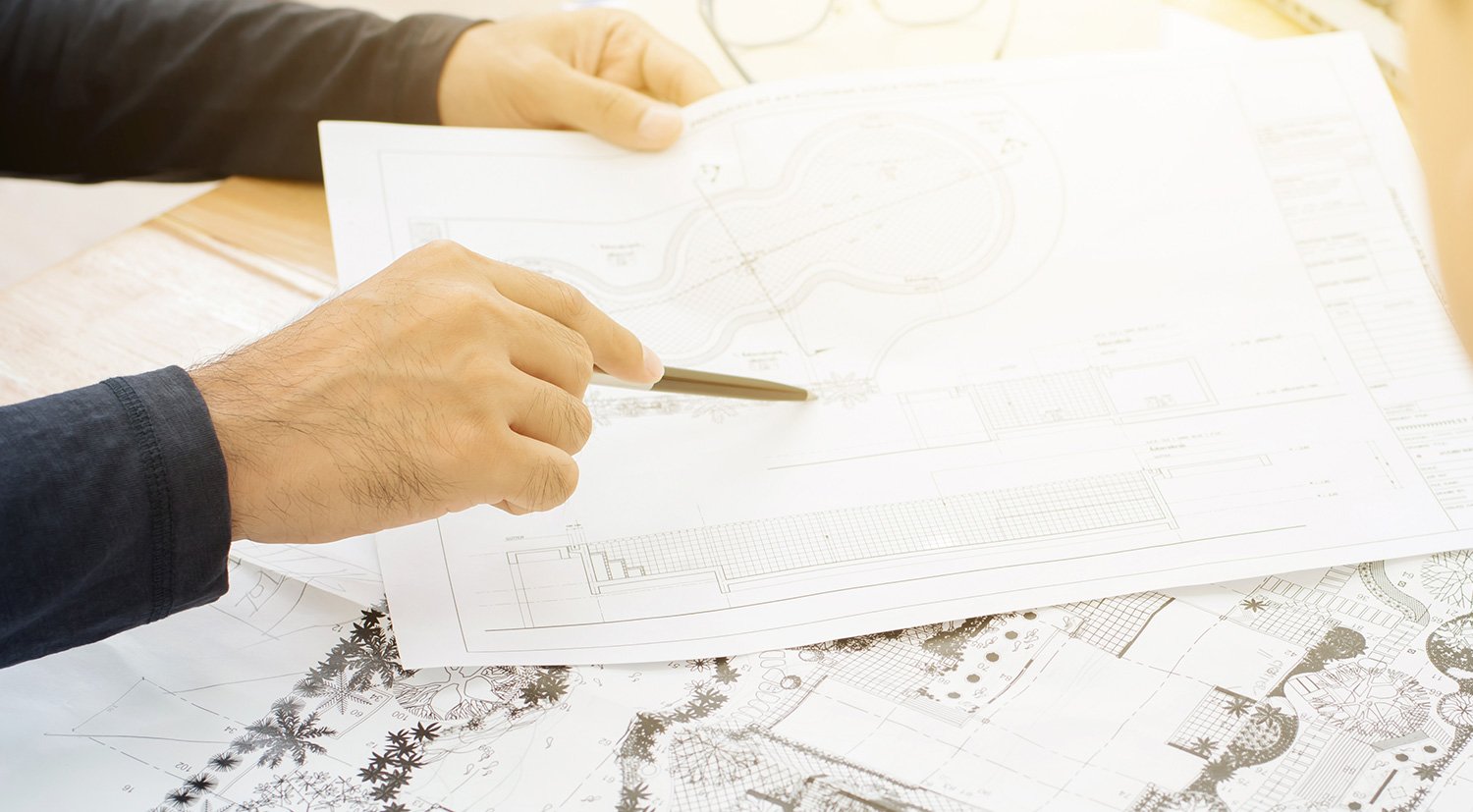 Close up view of a landscape architects hands holding a pen and pointing to a specific piece on a blue print design paper - links to the Why Get Independent Advice page