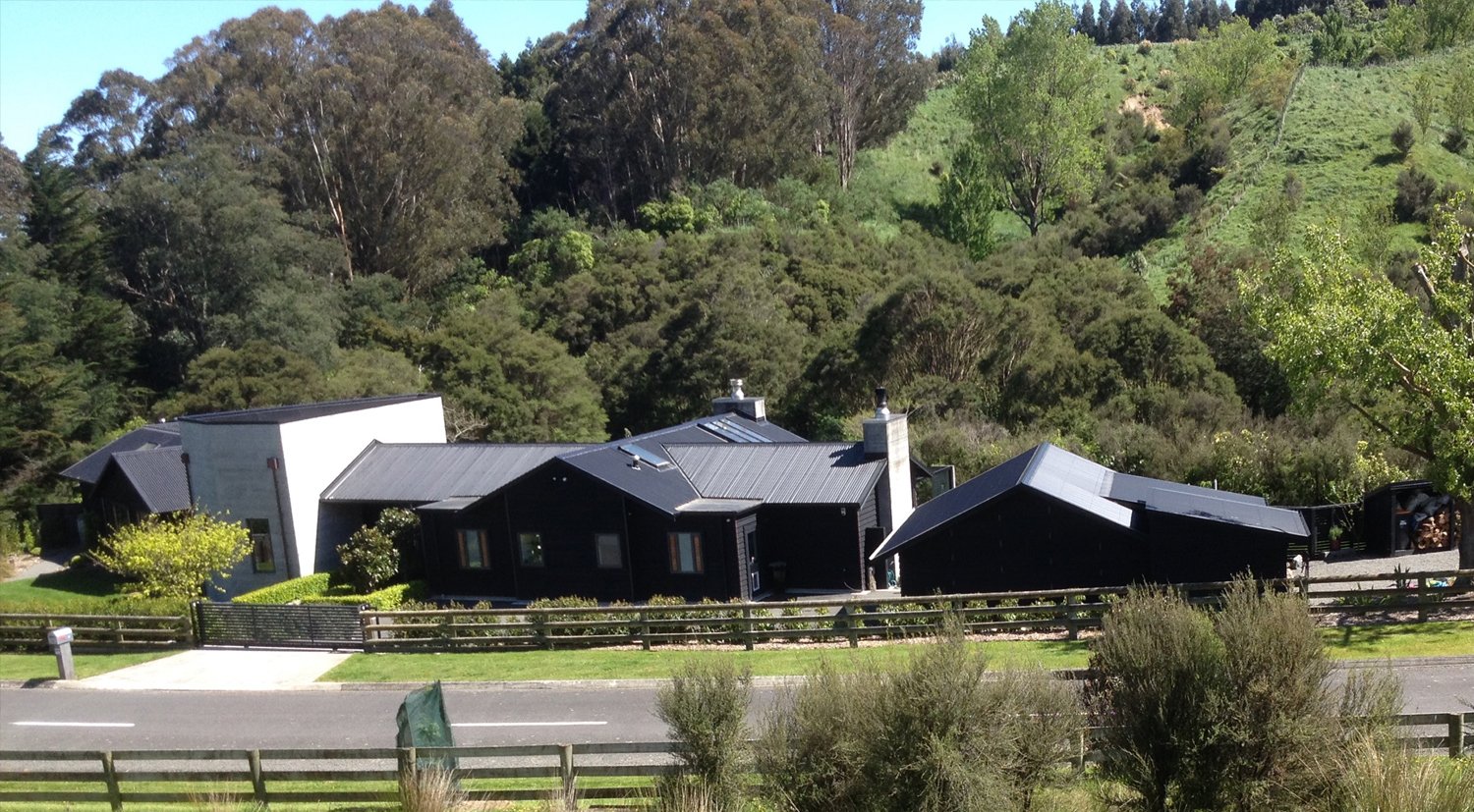 A rural house, modern and black with a hill and native bush behind it - links to Rural Septic Systems page