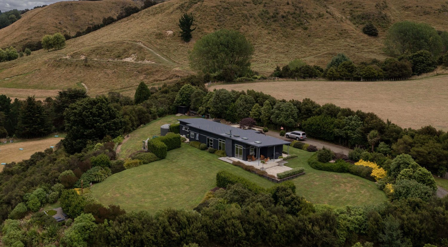 Aerial view of a rural house on a large lifestyle block with the house surrounded by a large circle of trees - links to the Case Studies page