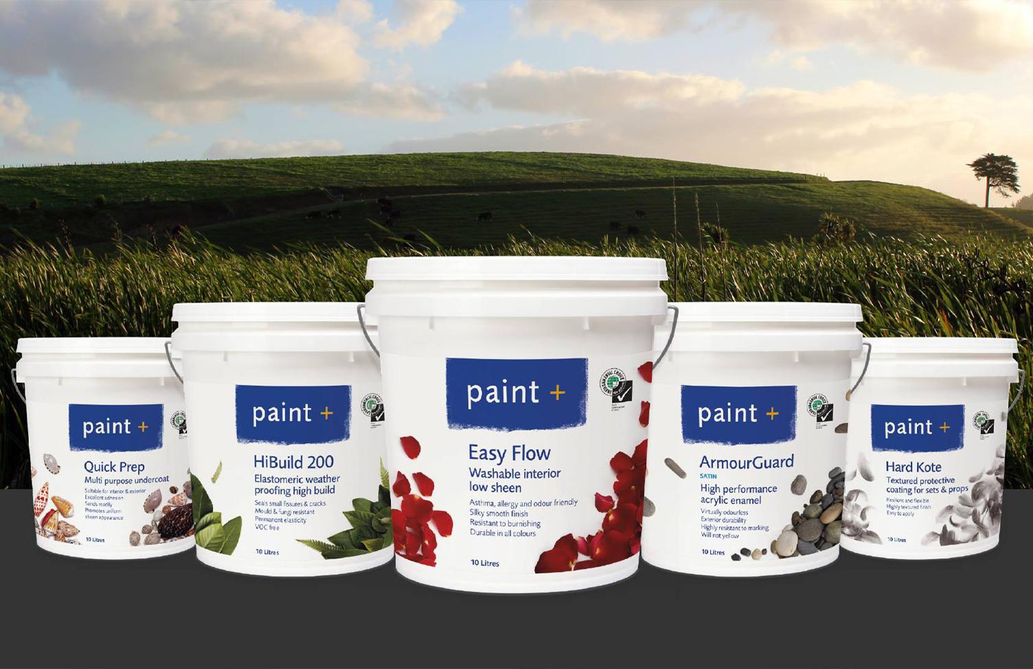Five different large buckets of paint from paint+ displayed with grass in the background