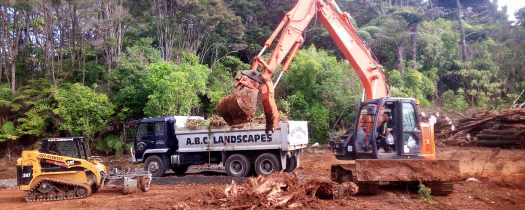 Small yellow levelling machinery being operated by an ABC Landscapes team member, pushing a pile of dirt out of the way to level the site
