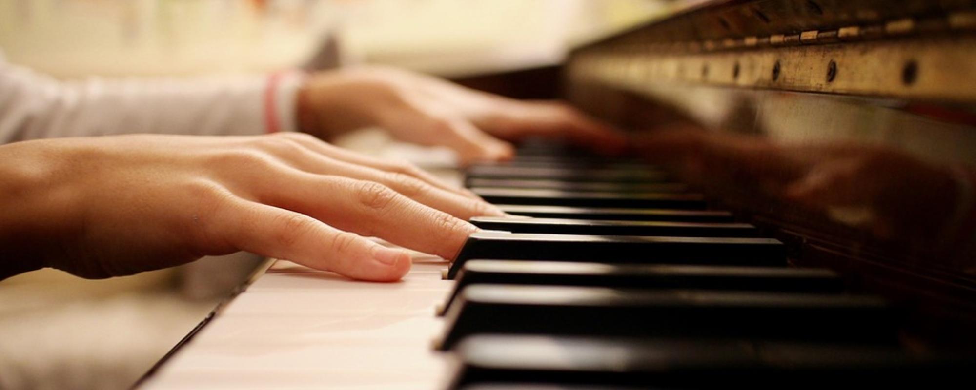 Close up of student's hands while playing the piano with prominent black and white keys