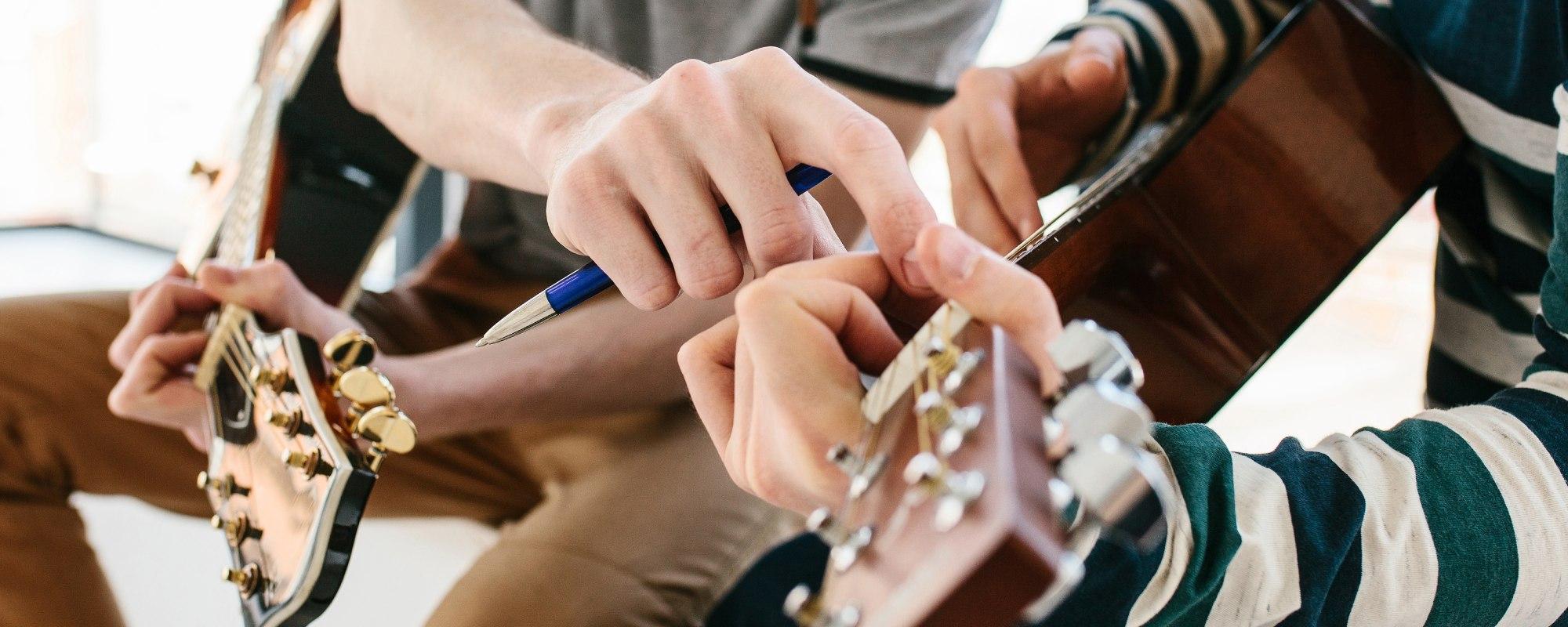 Music teacher and student with guitars while the teacher guides the student to the right note on their guitar