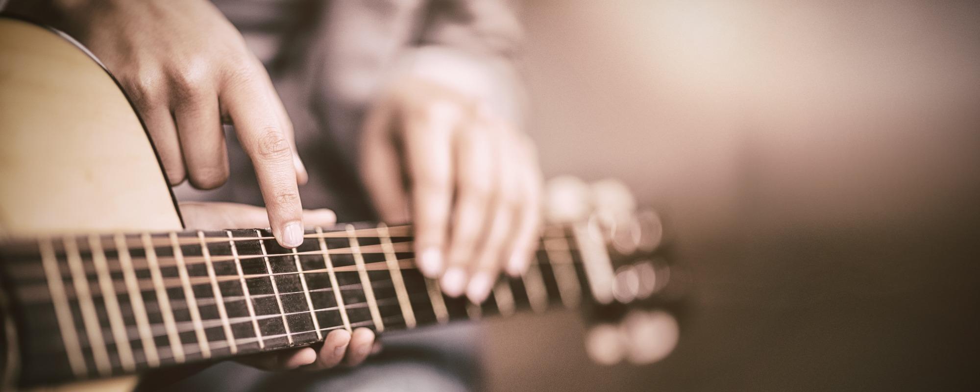 Music teacher and student sit together while the teacher points at the right note on the guitar