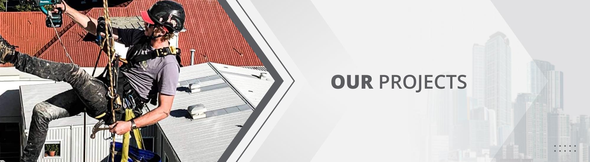 Abseiler on the side of a Waikato building, in a black helmet and safety gear while using a power tool on the building facade